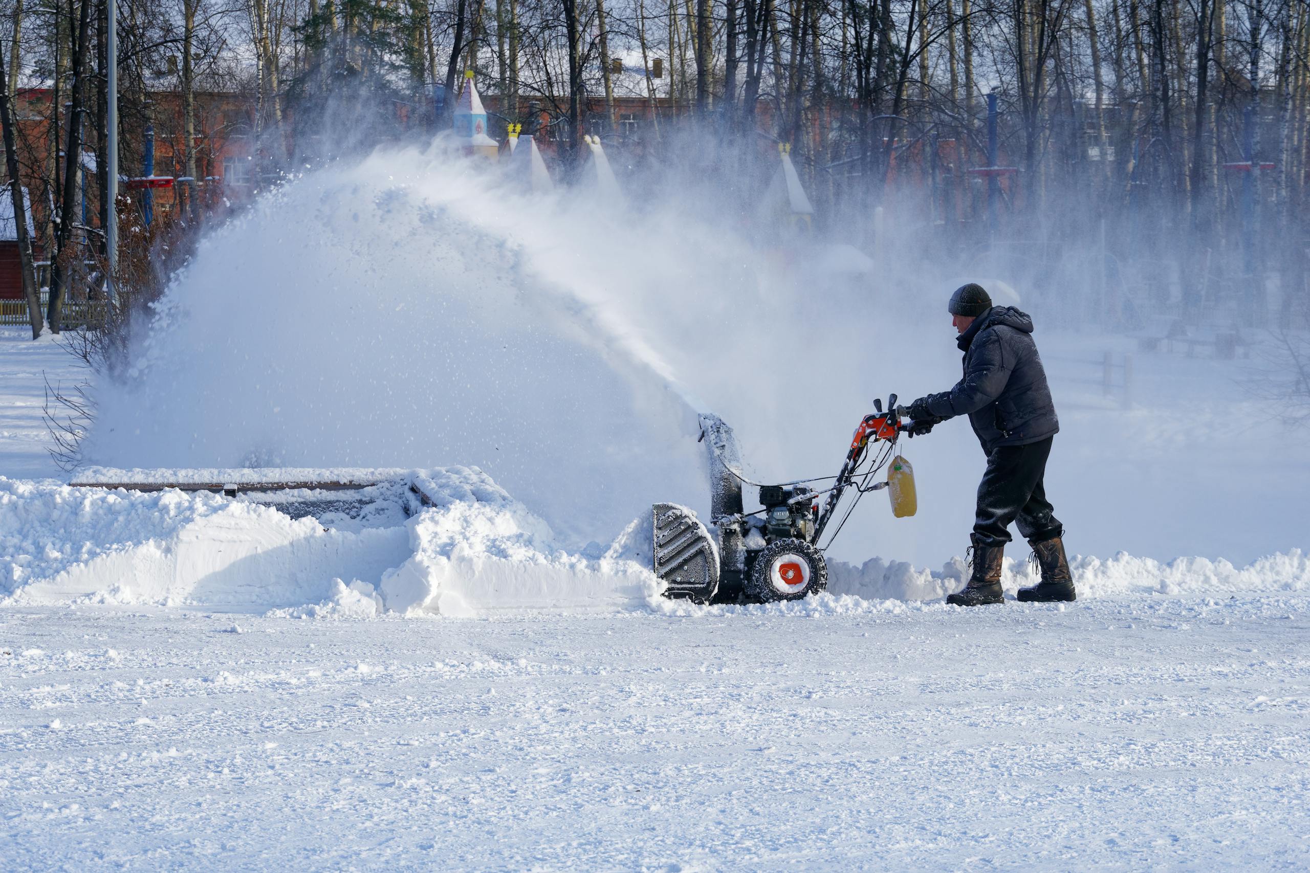 Full body man in warm clothes walking with snow thrower while cleaning yard in town